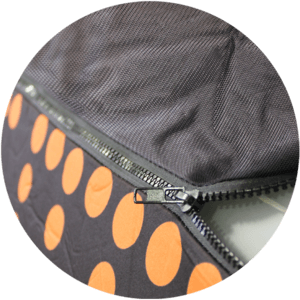 Close-up of a zipper on fabric featuring black and orange polka dots. The zipper is partially open, much like the hidden seams of inflatable furniture, offering a peek at the colorful material beneath.