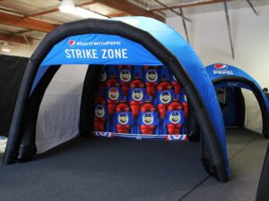 Inflatable blue Pepsi tent labeled STRIKE ZONE with emoji-themed graphics inside. The tent is set up indoors on a gray carpet, featuring Pepsi branding and logos.
