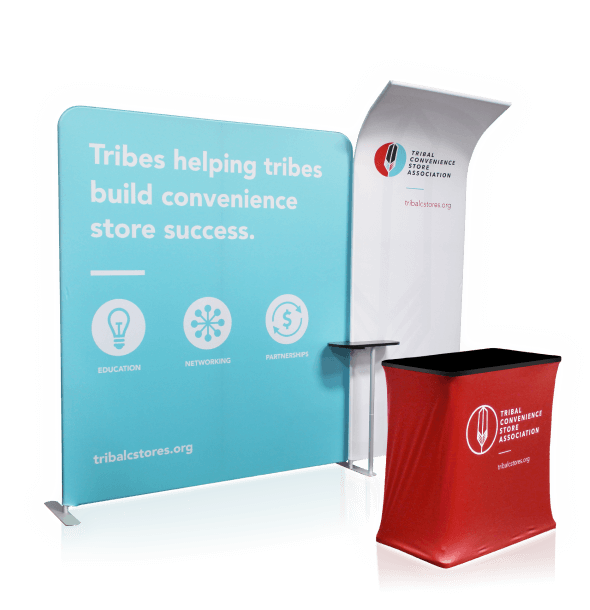 A portable trade show booth with a blue backdrop reads Tribes helping tribes build convenience store success, featuring icons for education, networking, and partnerships. A red podium cover displays the Tribal Convenience Store Association logo and website.