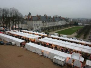 Aerial view of a market with rows of white tents, surrounded by historic buildings and bare trees. People browse the stalls on an overcast day.