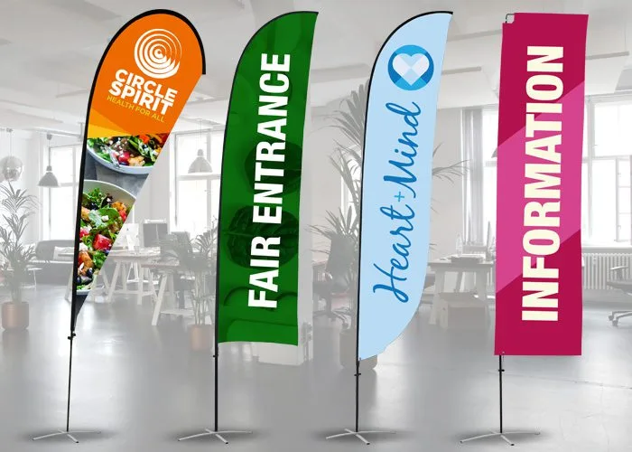 Four colorful vertical banners standing indoors: an orange one with CIRCLE SPIRIT, a green one saying FAIR ENTRANCE, a blue one with Heart & Mind, and a pink one labeled INFORMATION. The background shows a modern office space.