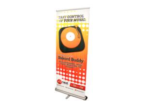 A retractable banner measuring 33.5" x 80" features a vibrant orange and white design with a vinyl record graphic to promote Rekord Buddy. The banner text reads "Take Control of Your Music," with event details neatly displayed at the bottom.