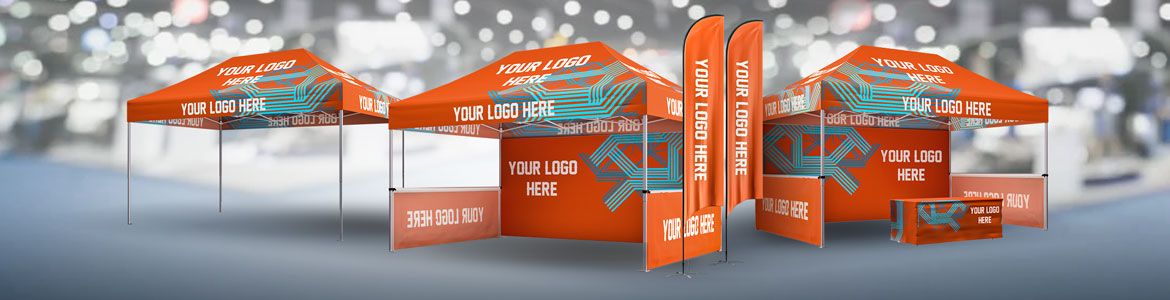 Three orange promotional tents with customizable logos are displayed. They feature bold text and graphics, surrounded by a blurred indoor background. Banners and counters accompany each tent setup.