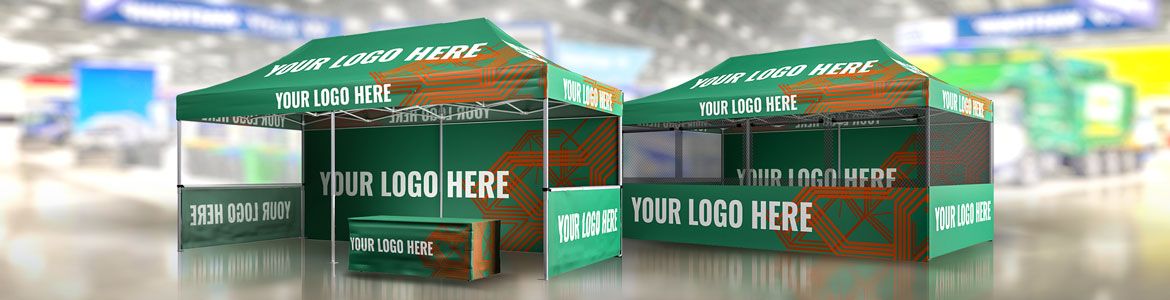 Two green promotional tents with the text YOUR LOGO HERE printed on them. One tent is open showing a table inside, while the other is closed. The background is a blurred indoor setting, suggesting an event or exhibition space.