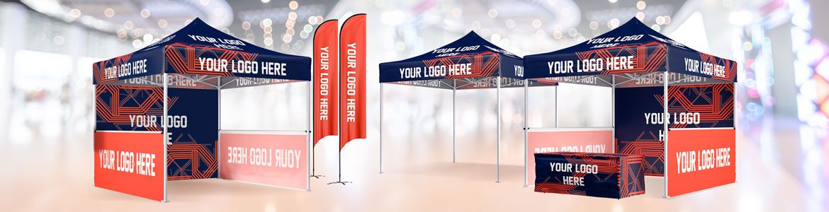 A promotional setup features two pop-up tents, a booth, a table, and two vertical banners. The designs are navy blue and red with abstract geometric patterns and the text Your Logo Here and Book Today.